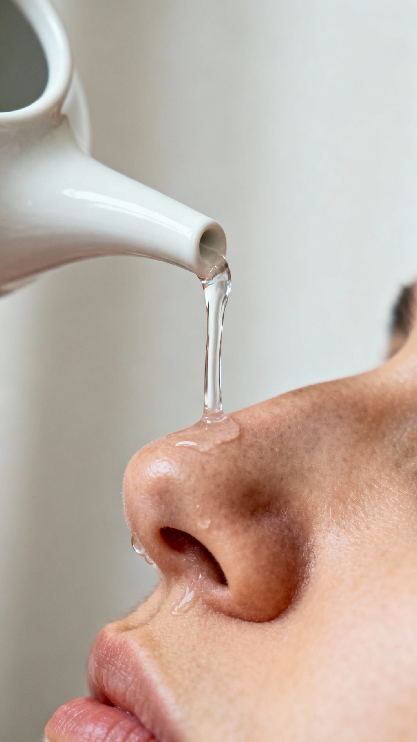 Closeup of neti pot pouring saline into nostril