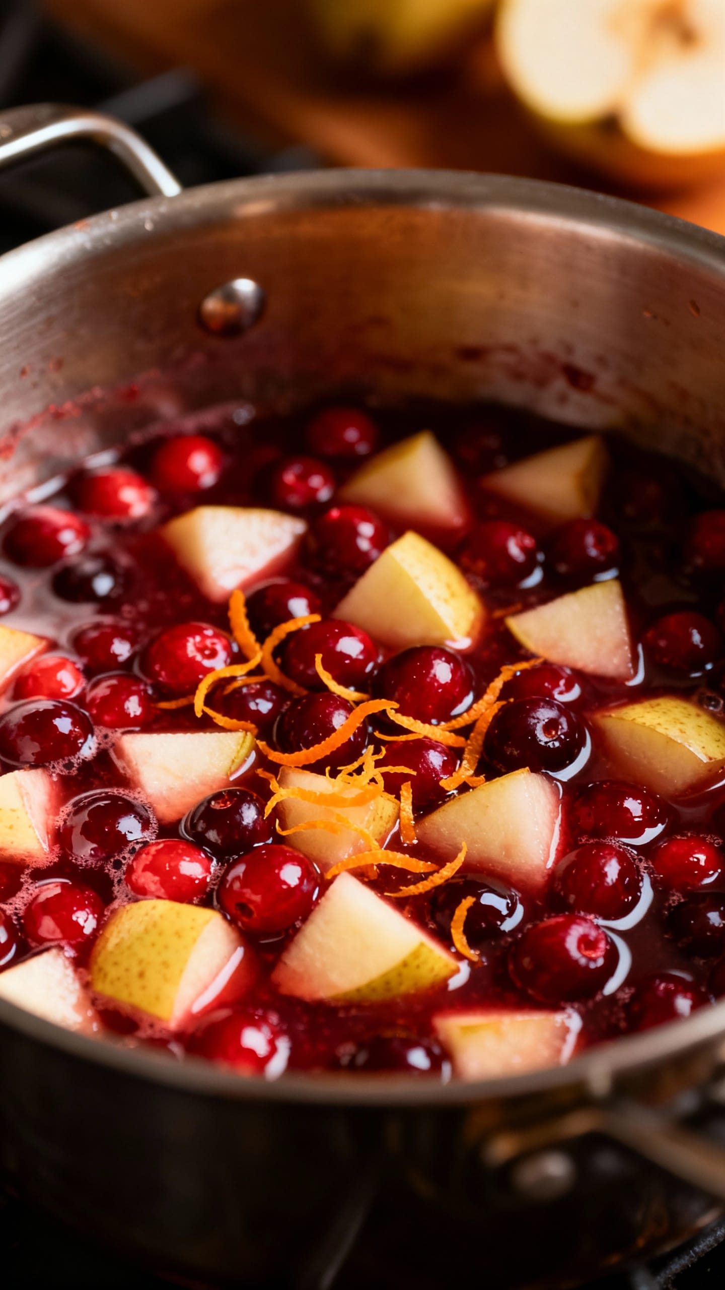 Closeup saucepan simmering cranberries and diced pears, orange zest